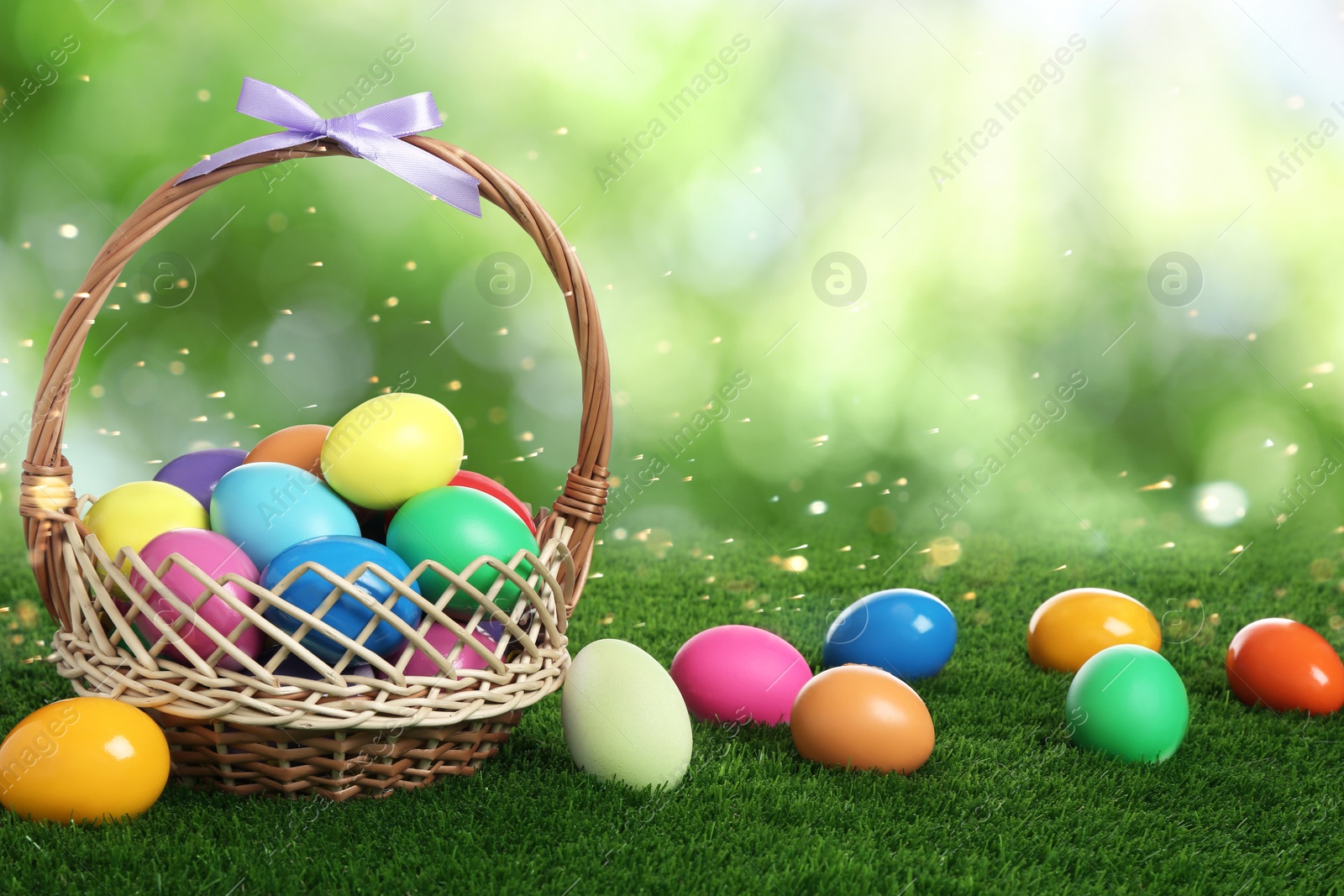 Image of Wicker basket with bright painted Easter eggs on green grass outdoors 