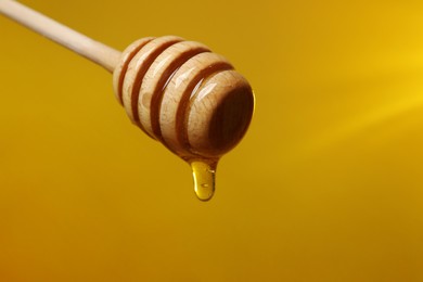 Photo of Pouring honey from dipper against golden background, closeup. Space for text