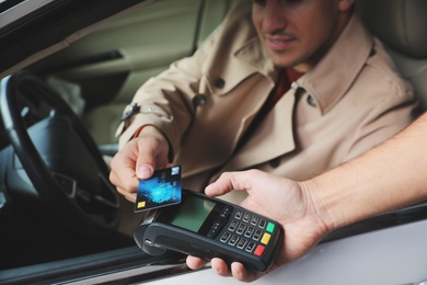 Photo of Man sitting in car and paying with credit card at gas station, closeup