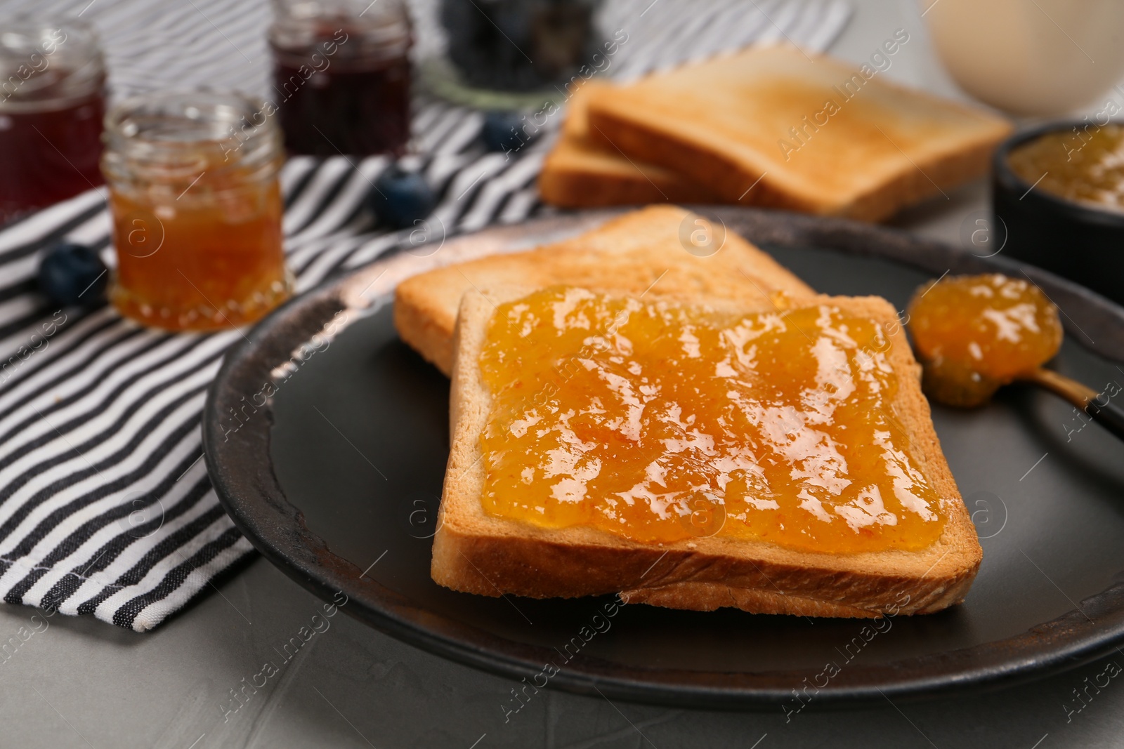 Photo of Toast with tasty orange jam served on grey table, closeup