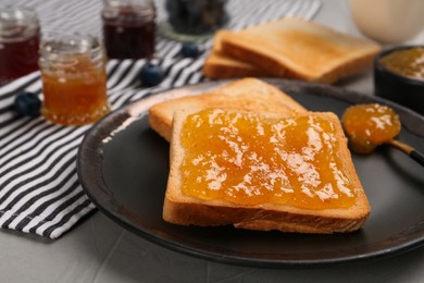 Photo of Toast with tasty orange jam served on grey table, closeup