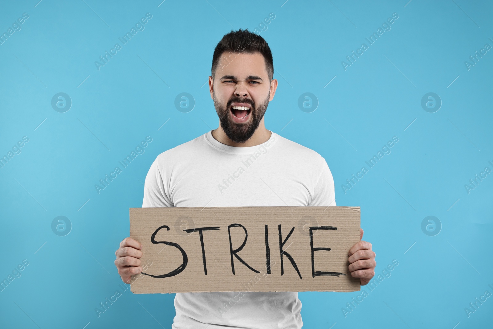 Photo of Angry man holding cardboard banner with word Strike on light blue background