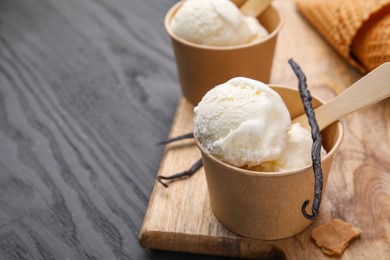 Photo of Paper cups with delicious ice cream and vanilla pods on grey wooden table, closeup. Space for text