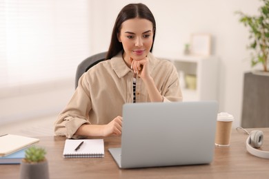 Young woman watching webinar at table in room