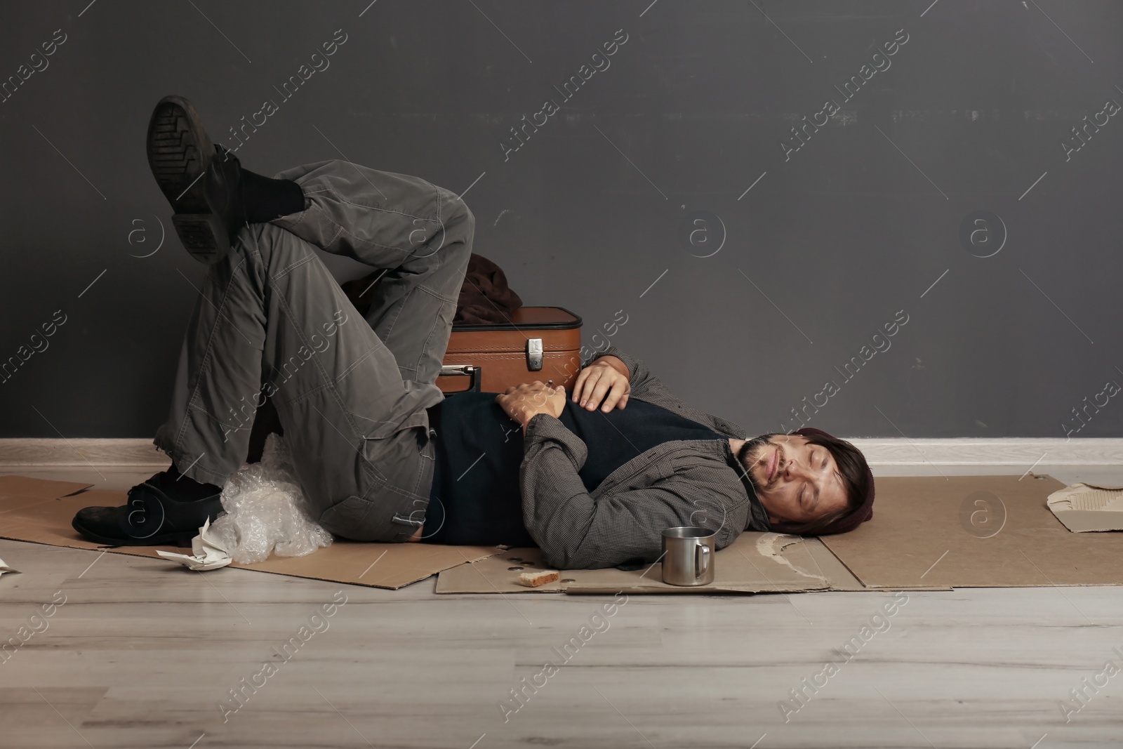 Photo of Poor homeless man sleeping on floor near dark wall