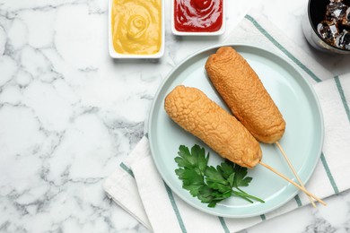 Photo of Delicious deep fried corn dogs with sauces on white marble table, flat lay. Space for text