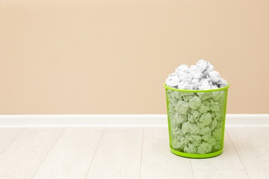 Photo of Metal bin with crumpled paper against color wall, space for text