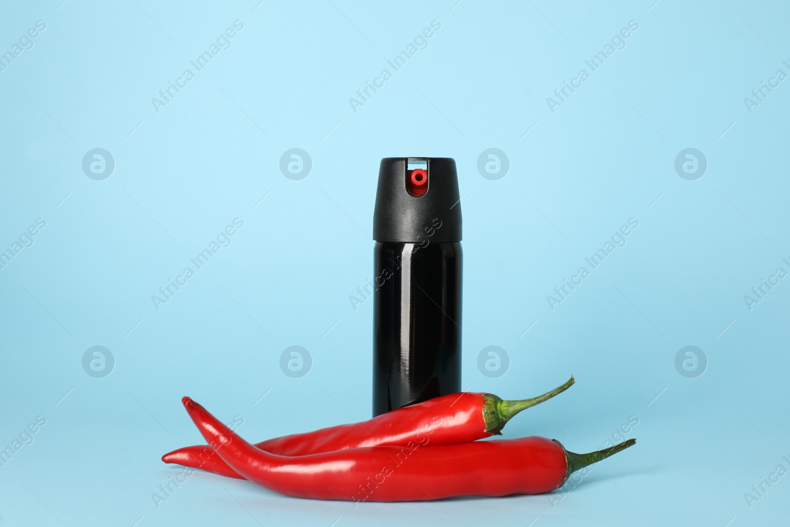 Photo of Bottle of gas pepper spray and fresh chili peppers on light blue background