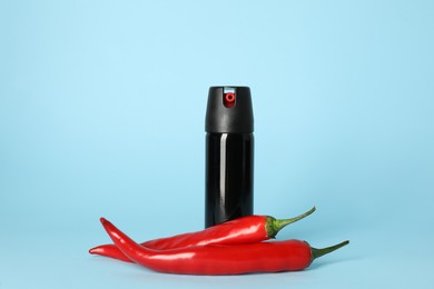 Bottle of gas pepper spray and fresh chili peppers on light blue background