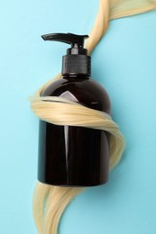 Photo of Shampoo bottle wrapped in lock of hair on light blue background, top view