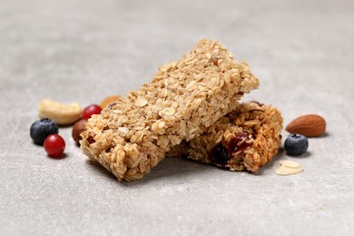 Photo of Tasty granola bars and ingredients on light grey table, closeup