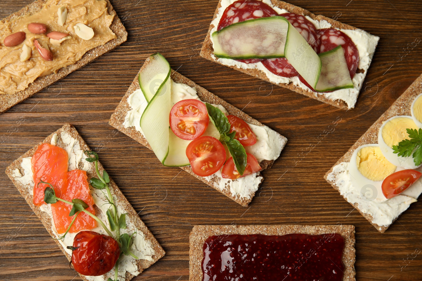 Photo of Fresh rye crispbreads with different toppings on wooden table, flat lay