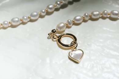 Elegant pearl necklace on white textured background, closeup