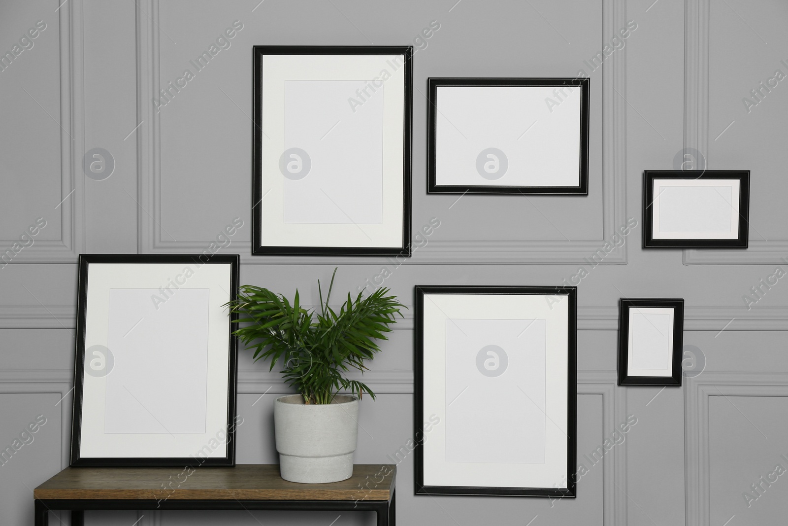 Photo of Empty frames hanging on grey wall near wooden table indoors