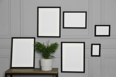 Photo of Empty frames hanging on grey wall near wooden table indoors