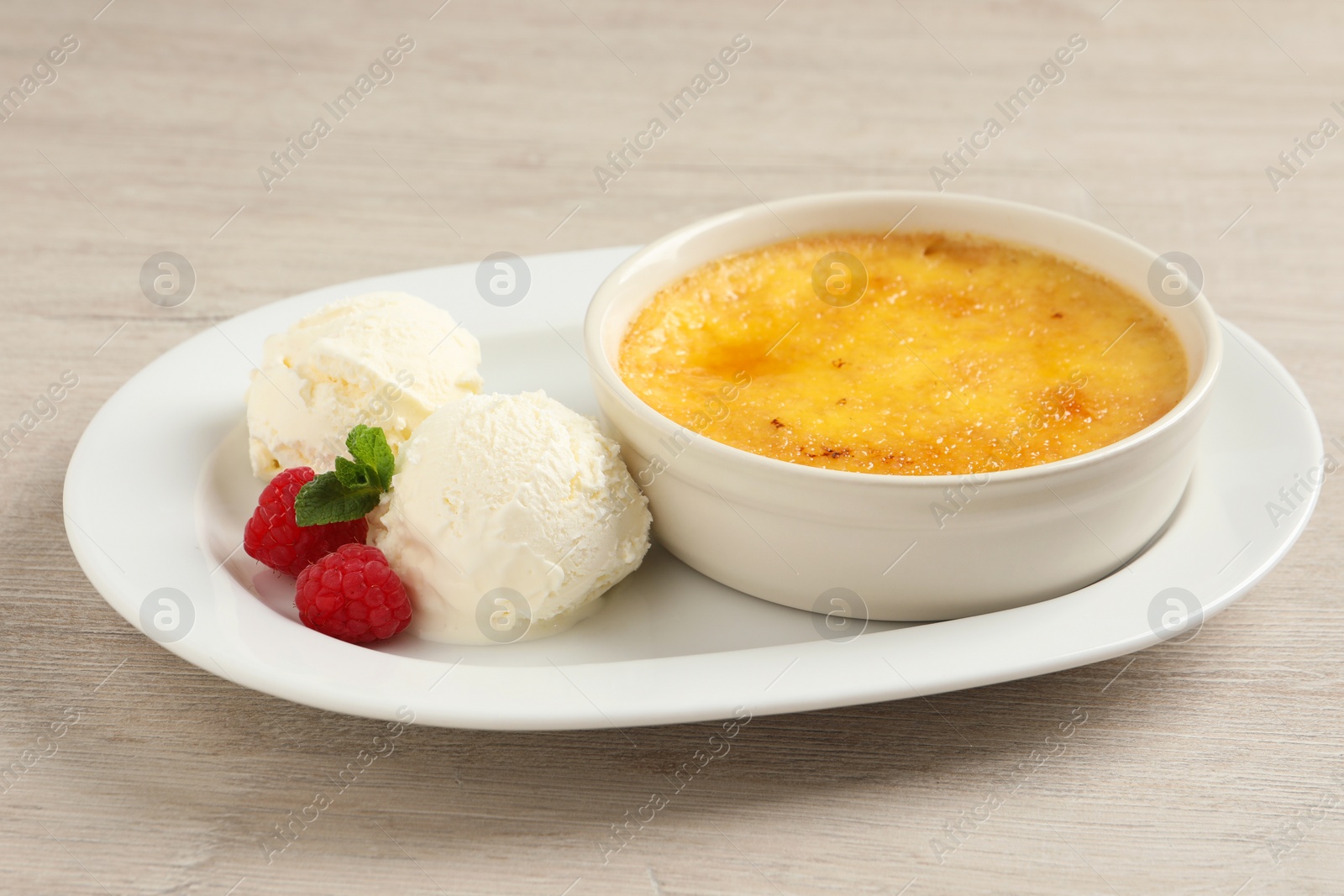Photo of Delicious creme brulee served with scoops of ice cream, fresh raspberries and mint on light wooden table