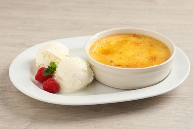 Delicious creme brulee served with scoops of ice cream, fresh raspberries and mint on light wooden table