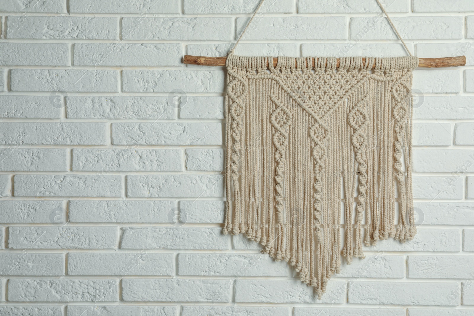 Photo of Beautiful macrame hanging on white brick wall, space for text. Decorative element