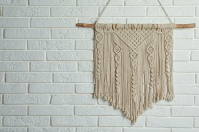 Photo of Beautiful macrame hanging on white brick wall, space for text. Decorative element