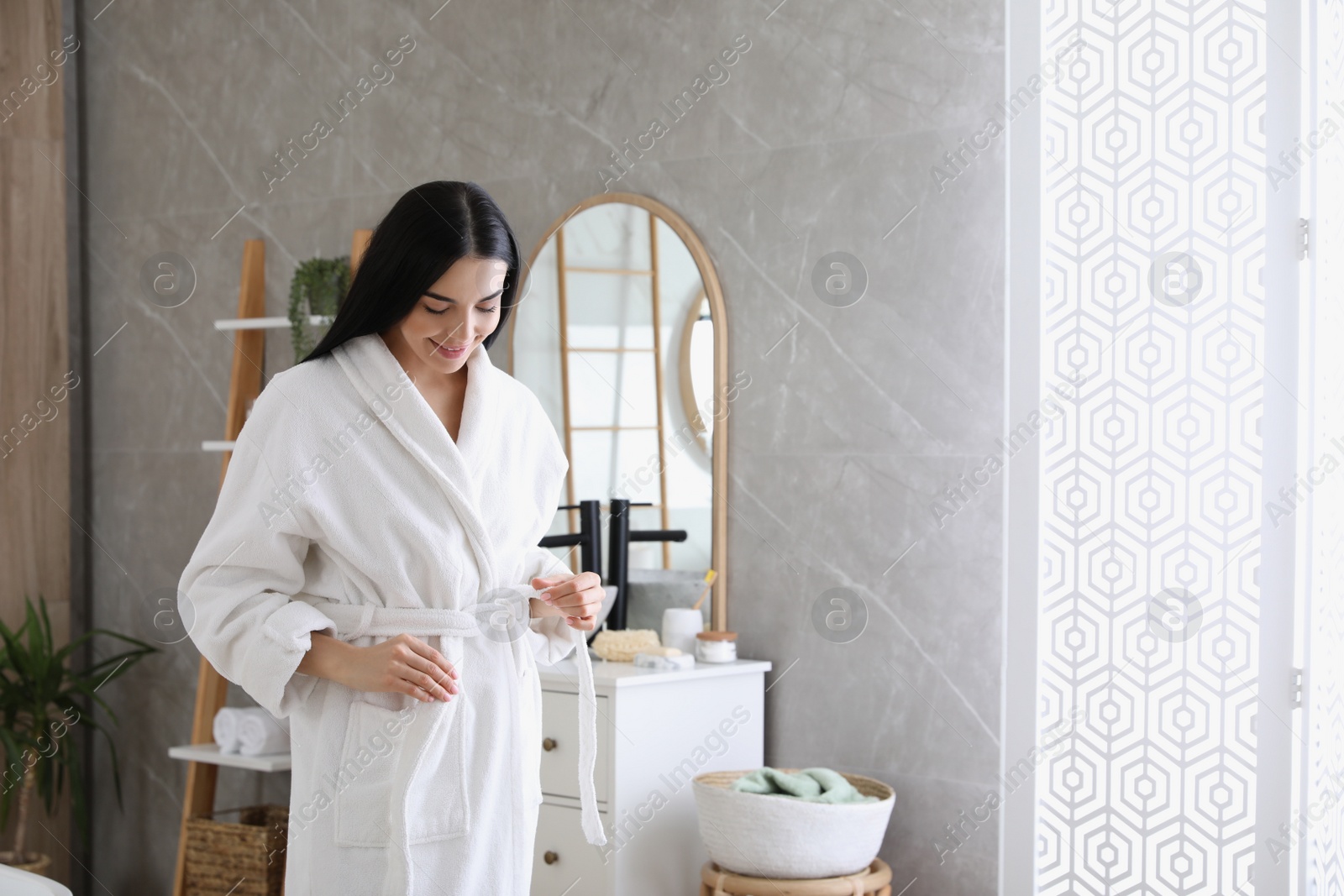 Photo of Beautiful young woman wearing soft white robe in bathroom