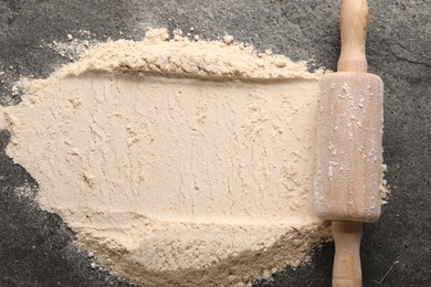 Scattered flour and rolling pin on grey textured table, top view