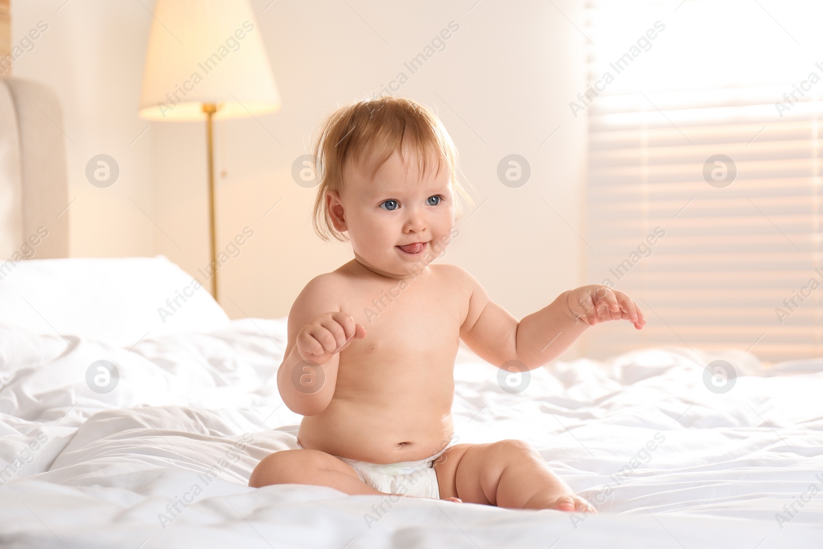 Photo of Cute little baby in diaper sitting on bed