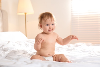 Photo of Cute little baby in diaper sitting on bed