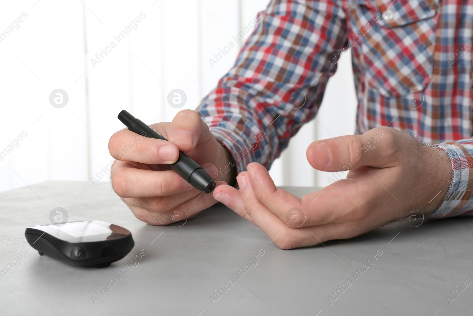 Photo of Man using lancet pen at table. Diabetes test