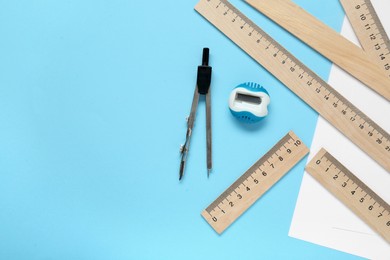 Different rulers, pencil sharpener and compass on light blue background, flat lay. Space for text