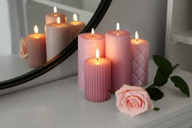 Photo of Burning candles and rose on white console table near mirror