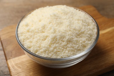 Photo of Glass bowl with grated parmesan cheese on wooden table, closeup