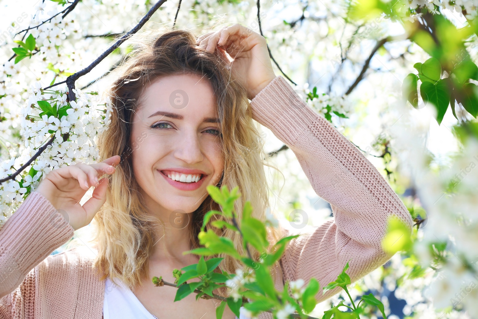 Photo of Attractive young woman posing near blossoming tree on sunny spring day