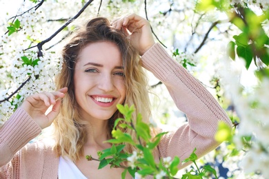 Photo of Attractive young woman posing near blossoming tree on sunny spring day