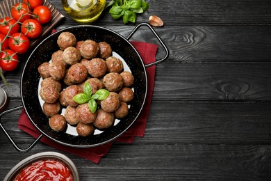 Photo of Tasty cooked meatballs with basil on black wooden table, flat lay. Space for text