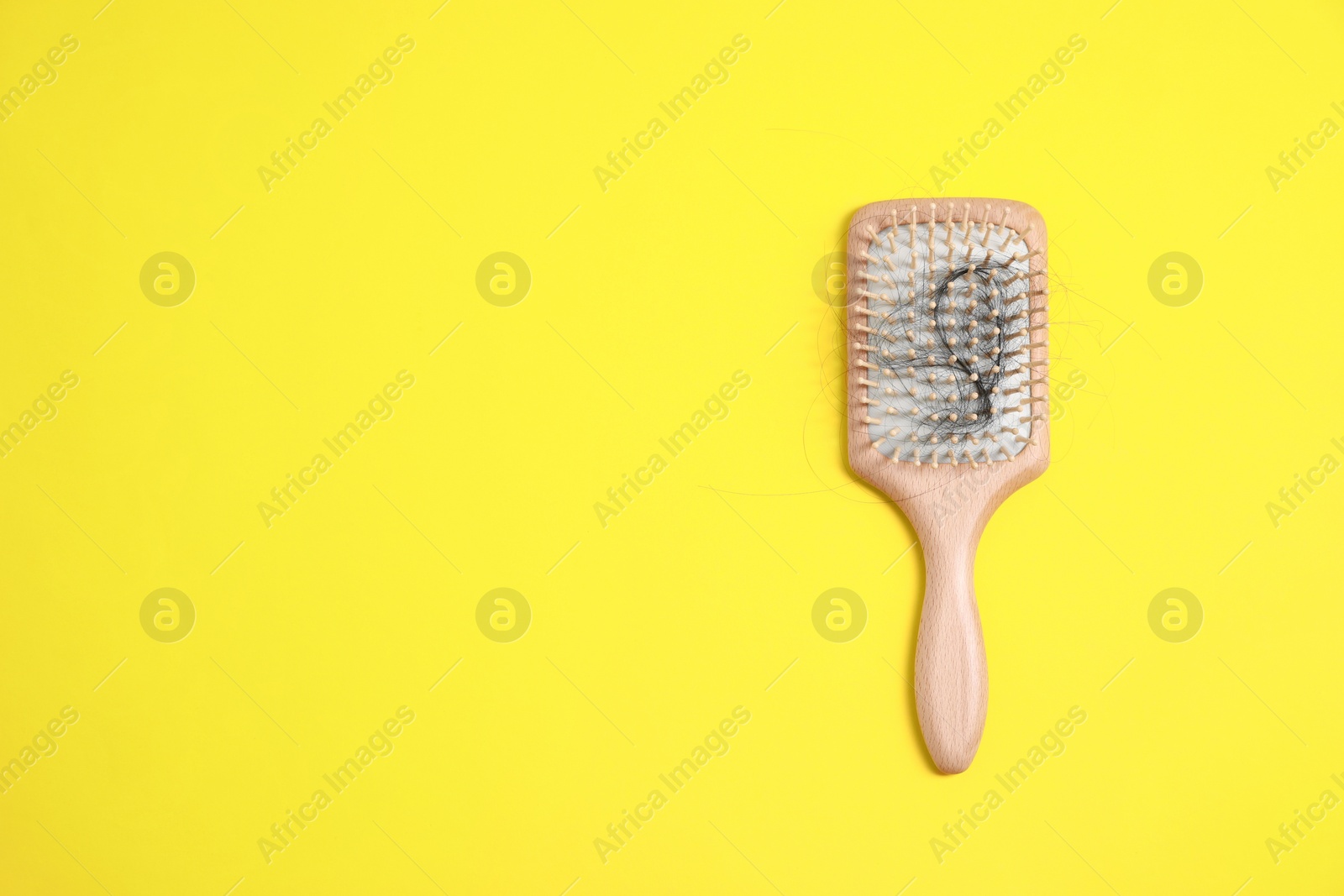 Photo of Wooden brush with lost hair on yellow background, top view. Space for text