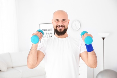 Photo of Overweight man doing exercise with dumbbells at home