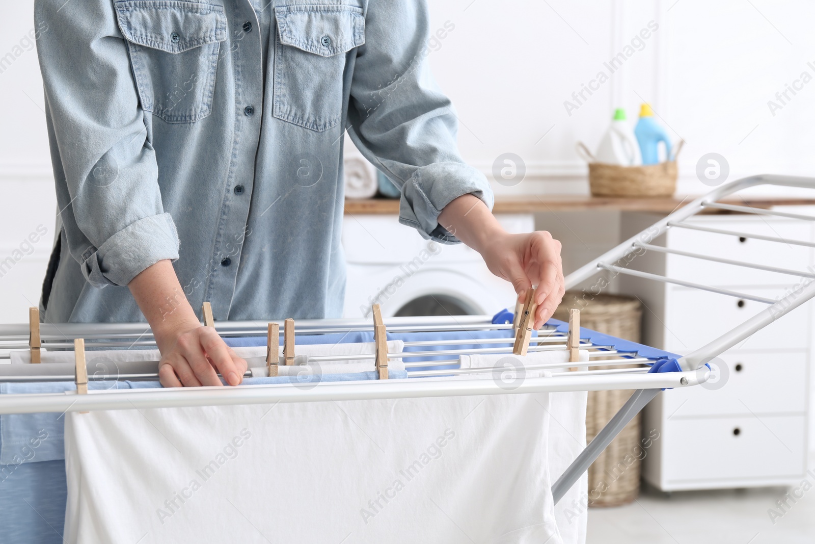 Photo of Woman hanging clean laundry on drying rack in bathroom, closeup