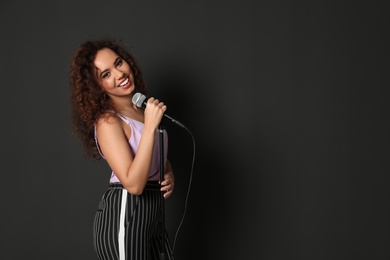 Curly African-American woman in stylish clothes posing with microphone on black background. Space for text