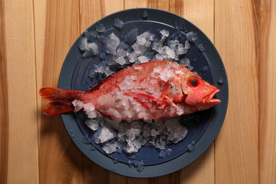 Fresh raw fish with ice on wooden table, top view