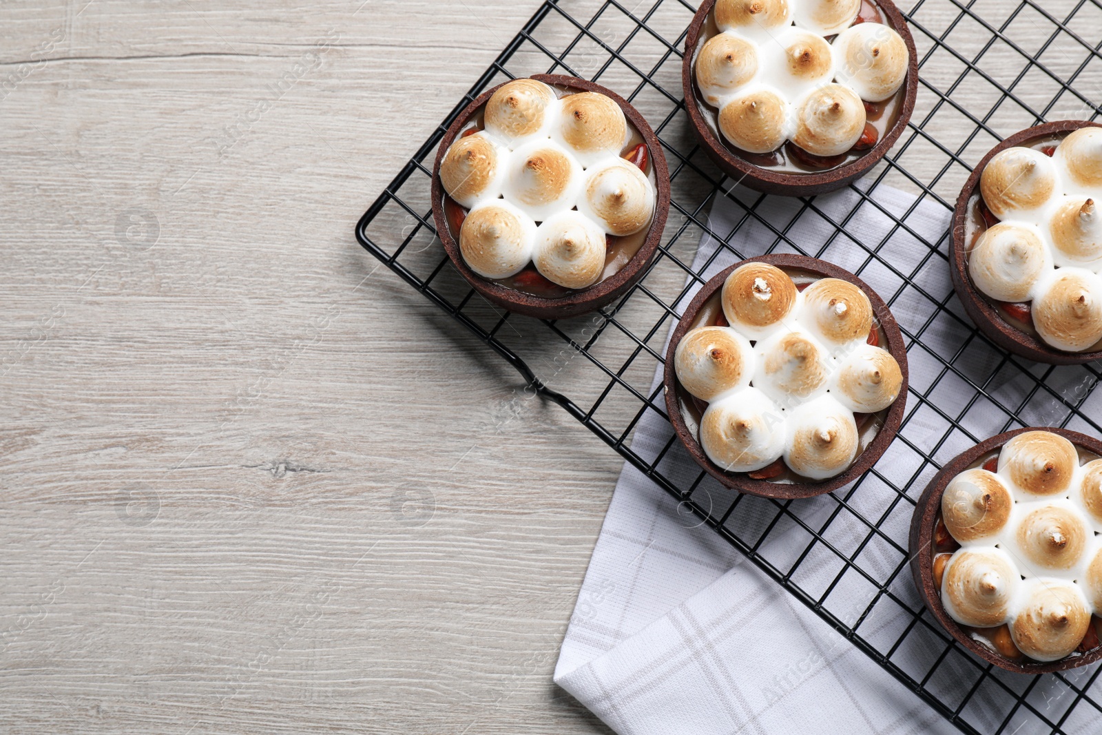 Photo of Delicious salted caramel meringue tarts on light wooden table, flat lay. Space for text