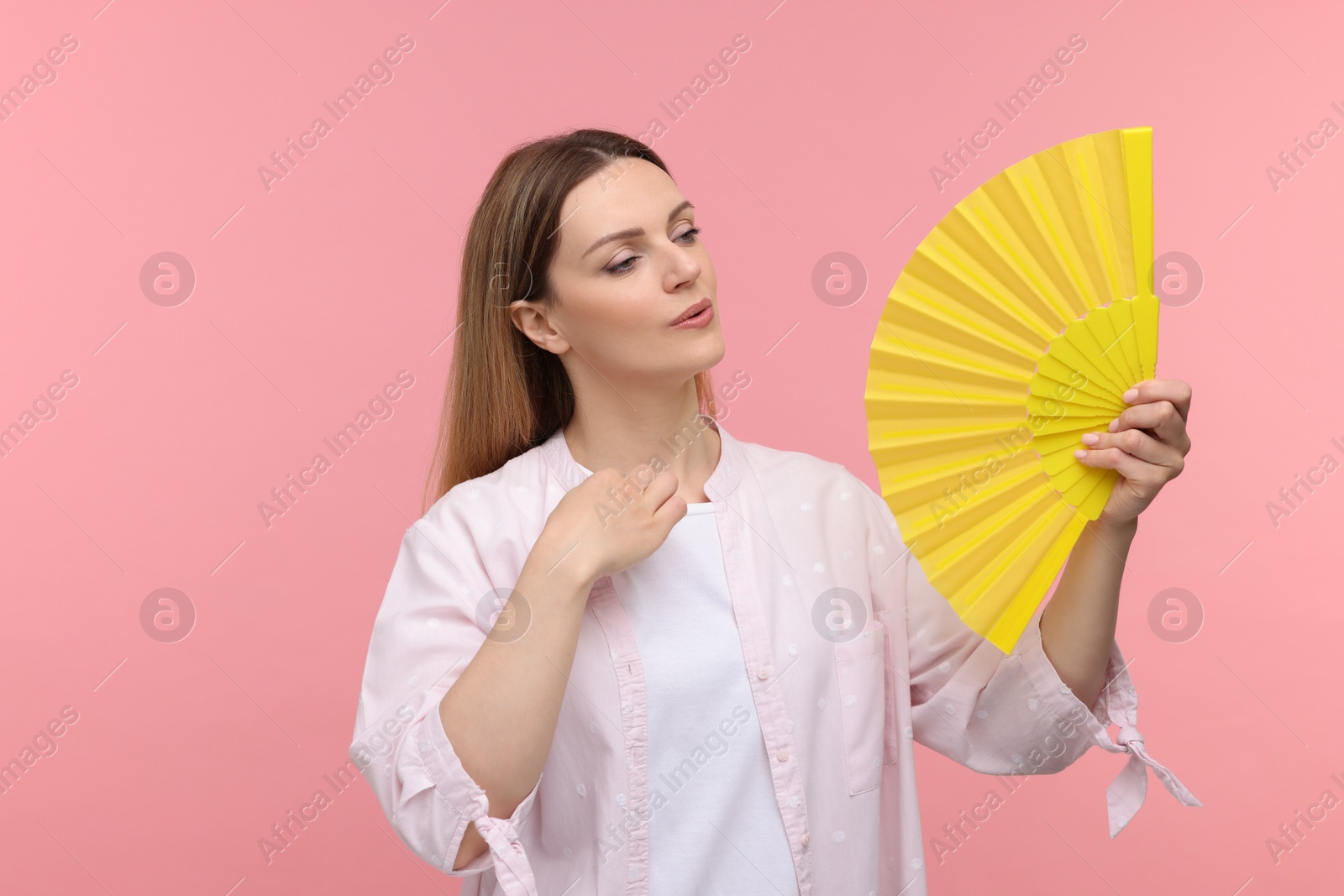 Photo of Beautiful woman waving yellow hand fan to cool herself on pink background