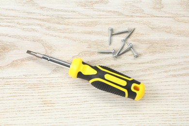 Photo of Screwdriver with yellow handle and screws on white wooden table, flat lay