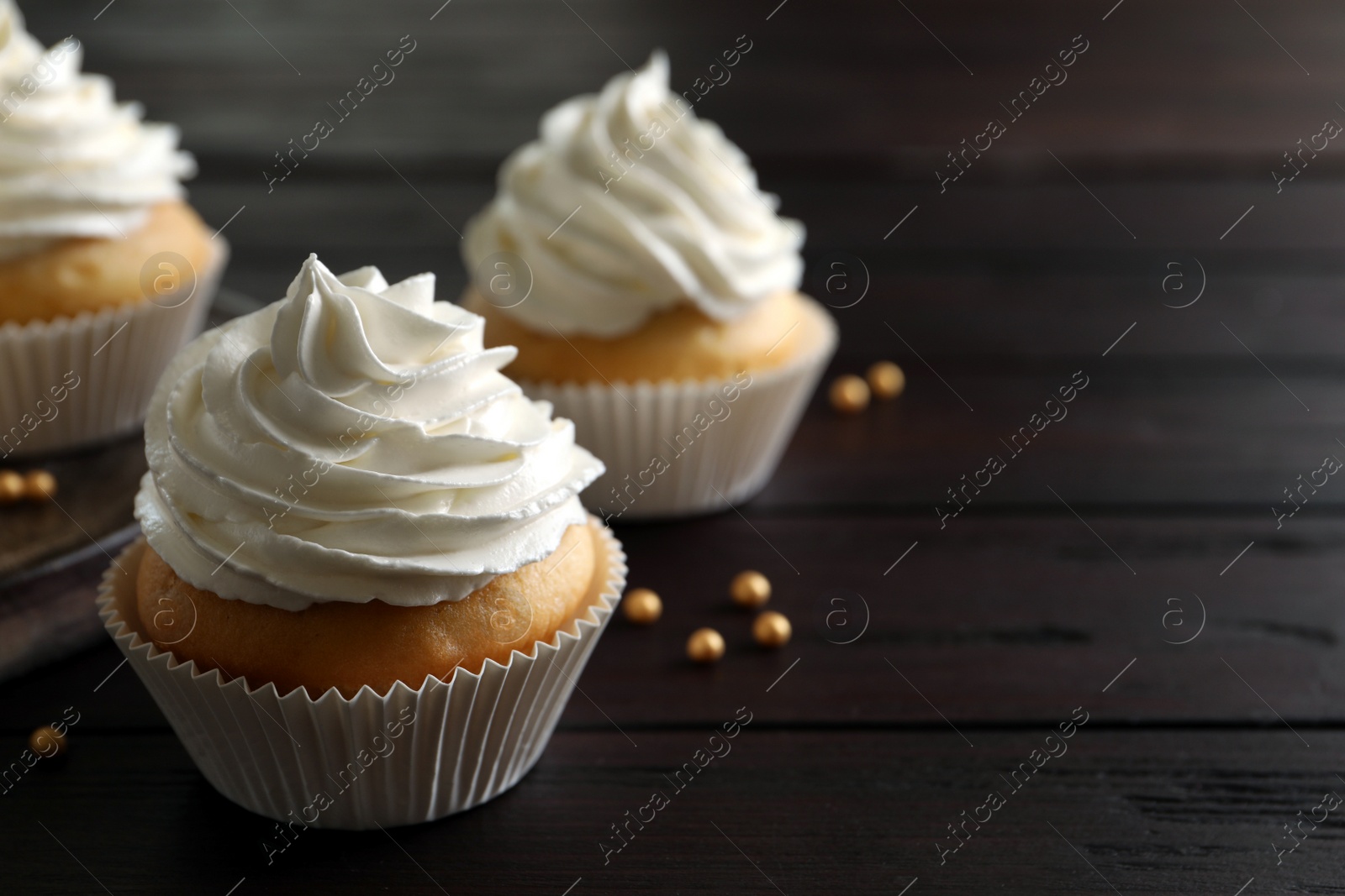 Photo of Delicious cupcakes with white cream on wooden table, closeup. Space for text