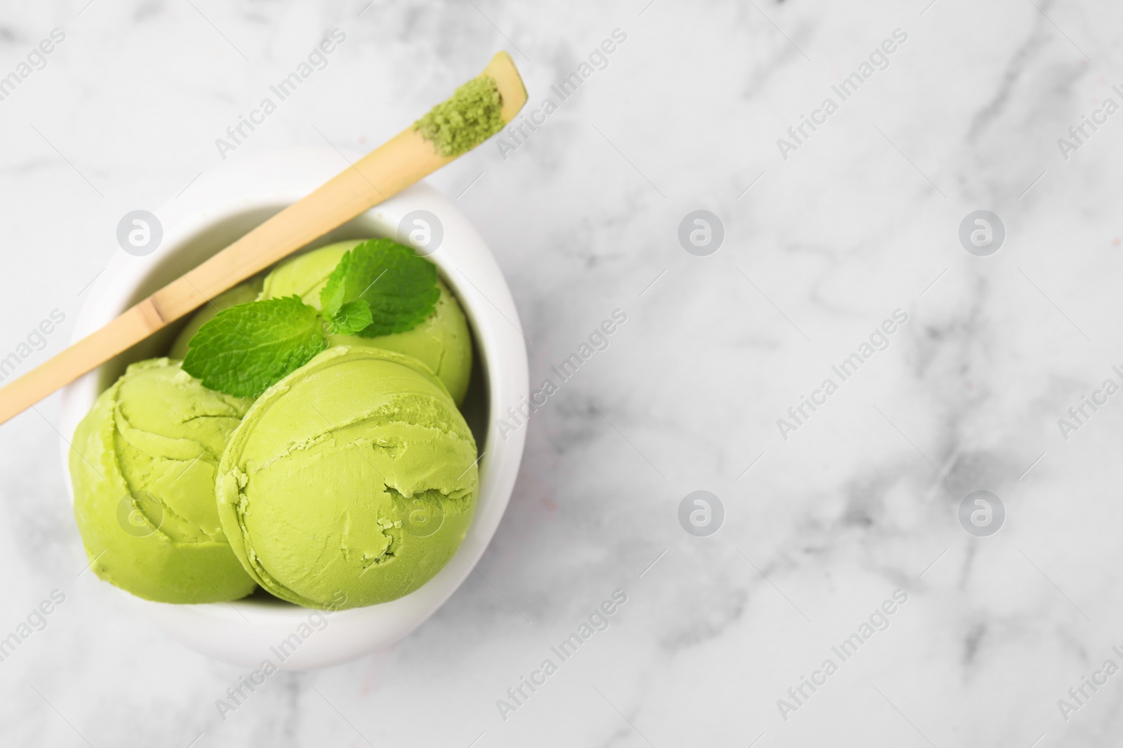 Photo of Tasty matcha ice cream in bowl and spoon with powder on white marble table, top view. Space for text