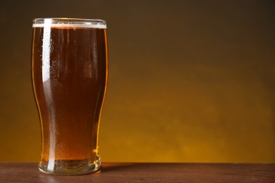 Photo of Glass with fresh beer on wooden table against dark background, closeup. Space for text