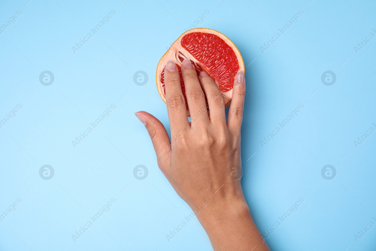 Photo of Young woman touching half of grapefruit on blue background, top view. Sex concept