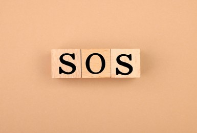Photo of Abbreviation SOS made of wooden cubes on light brown background, top view