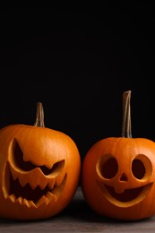 Photo of Scary jack o'lanterns made of pumpkins on wooden table against black background, space for text. Halloween traditional decor