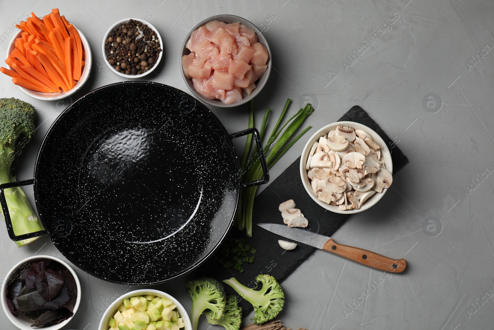 Photo of Wok pan, chicken and other products on light grey table, flat lay