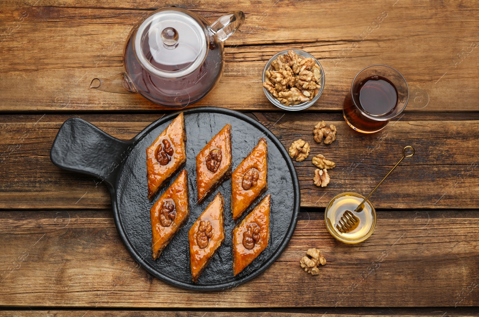 Photo of Delicious sweet baklava with walnuts, honey and hot tea on wooden table, flat lay